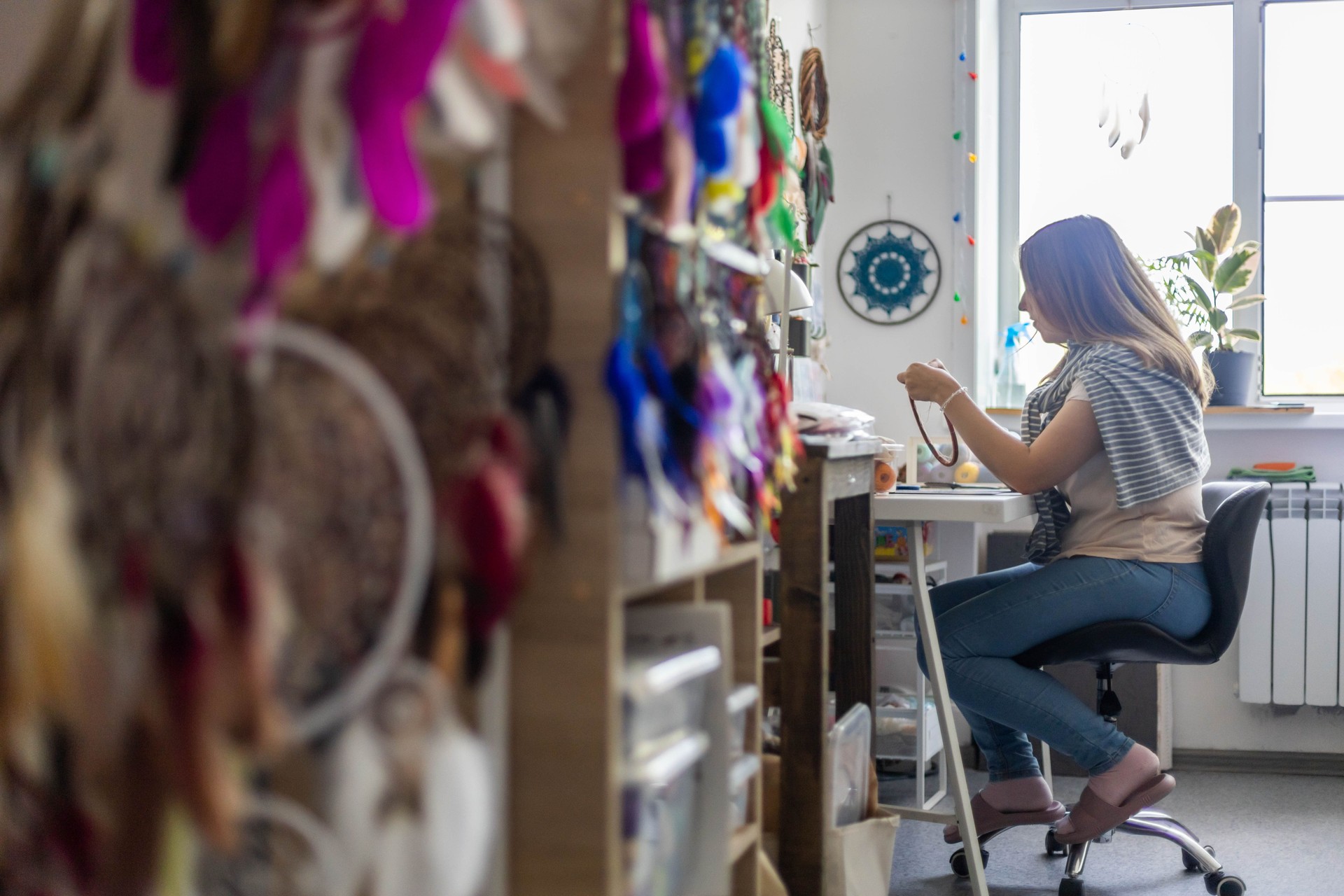 Female master creating Dreamcatcher working at workshop with feathers and materials